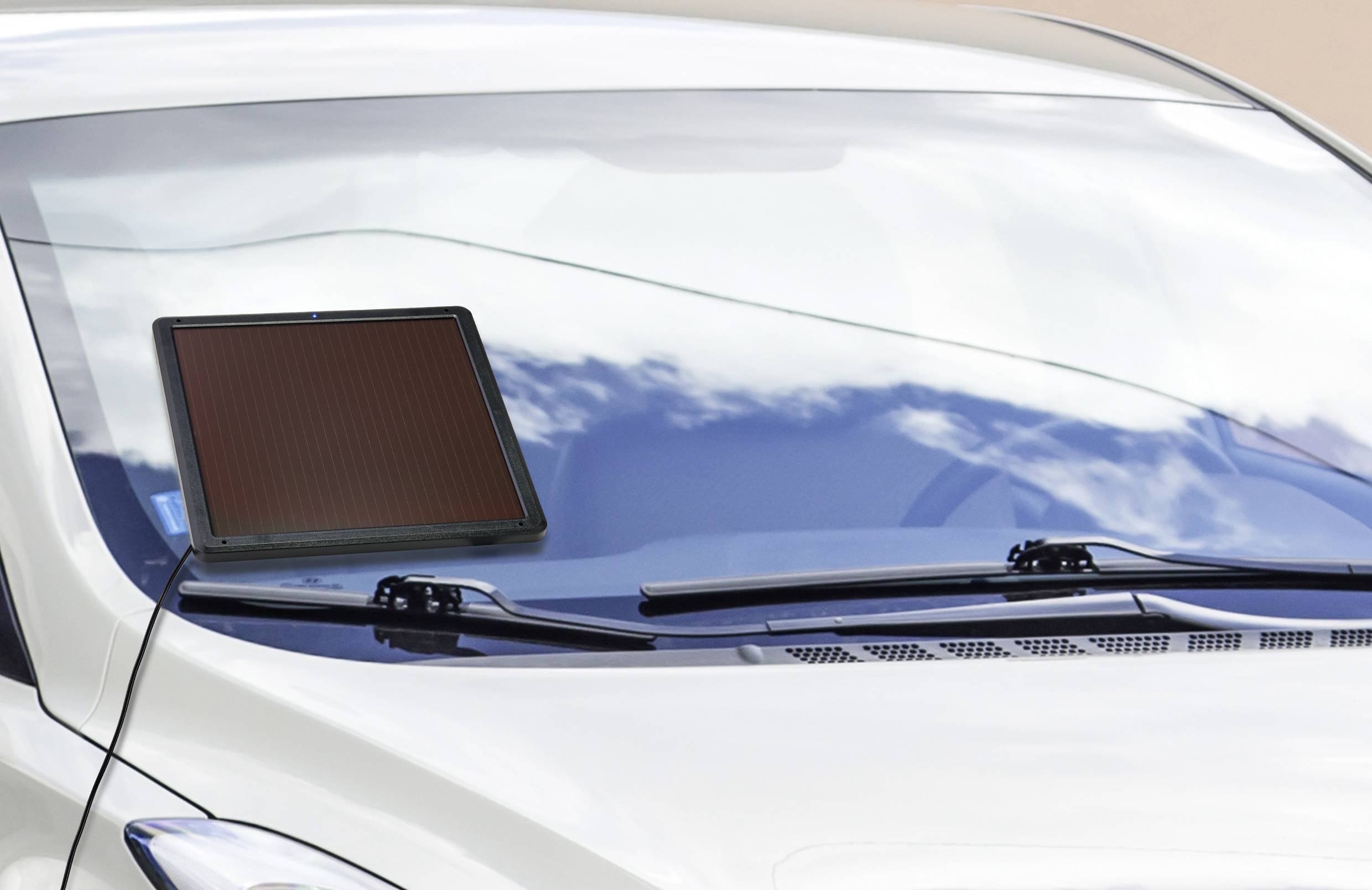 Ein Solarpanel auf der Windschutzscheibe eines Autos lädt ein Gerät auf, während es in der Sonne geparkt ist.