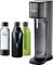 Sodastream-Maschine mit 'Sodapop'-Aufschrift und drei Glasflaschen: eine transparent, eine schwarze mit schwarzem Überzug, eine schwarze mit grünem Überzug.