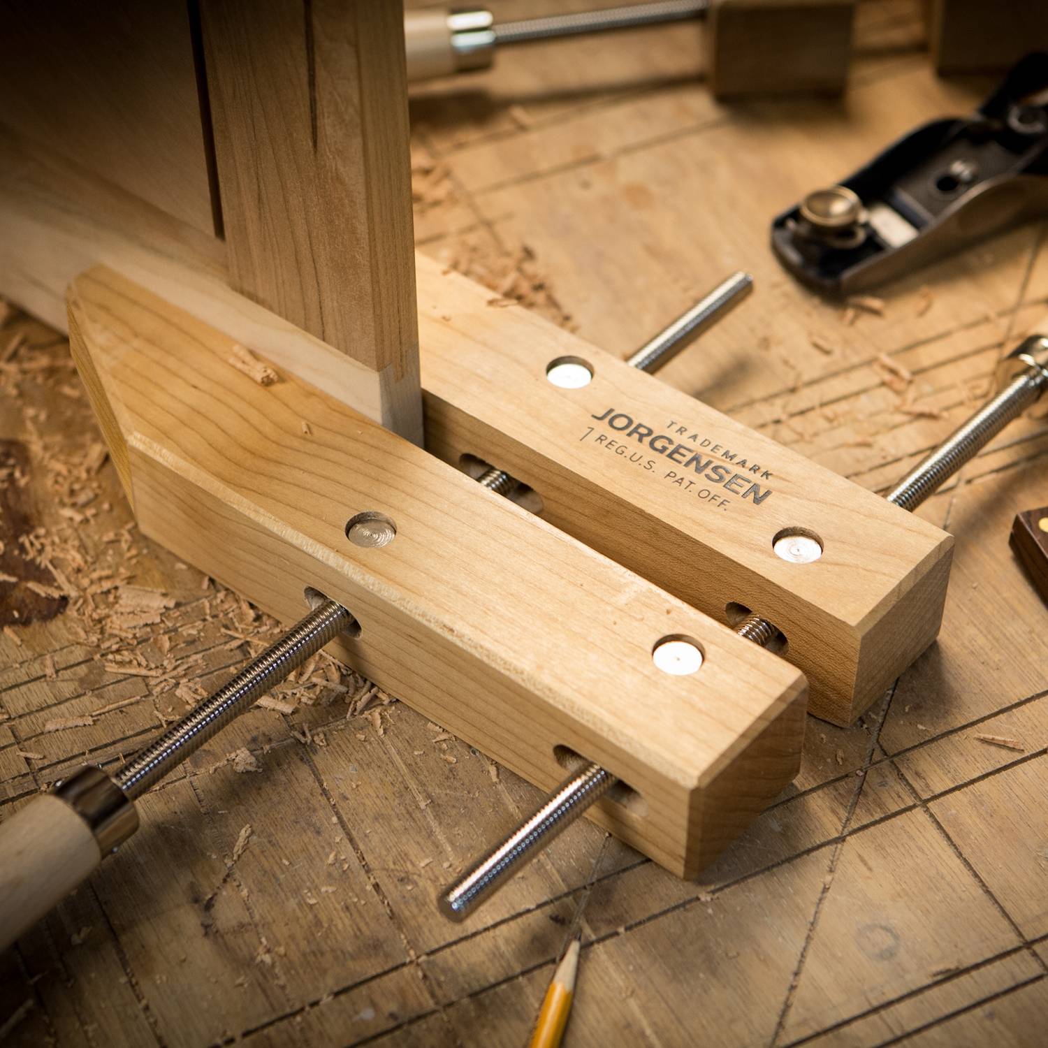 Holzwerkbank mit Schraubzwingen, die Holzstücke fixieren; Späne und ein Hobel umgeben die Konstruktion.