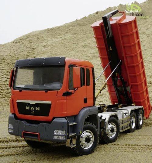 Ein roter Lastwagen mit gekippter Ladefläche steht auf einem Sandhügel in einer Baustellenszene.