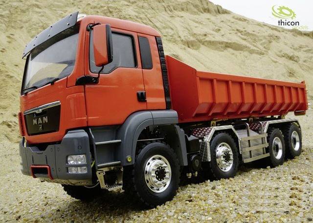 Ein roter Lastwagen steht auf kiesigem Boden vor einem Sandhügel. Im Hintergrund ist ein Logo zu erkennen.