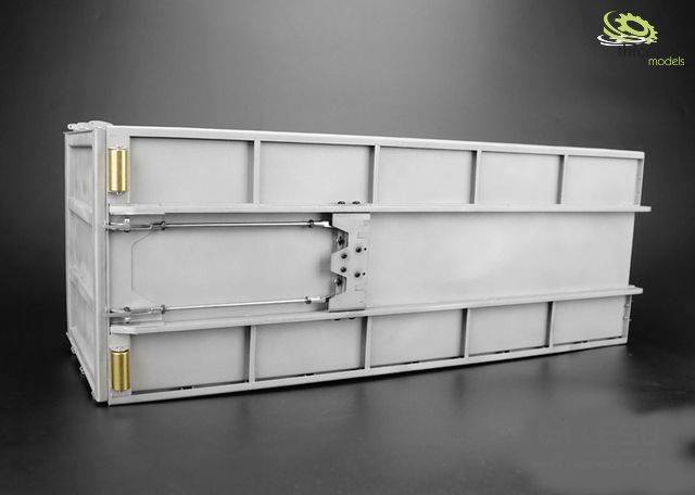 Ein graues, längliches Metallgehäuse mit Schrauben und Scharnieren auf einem dunklen Hintergrund, möglicherweise ein technisches Bauteil.