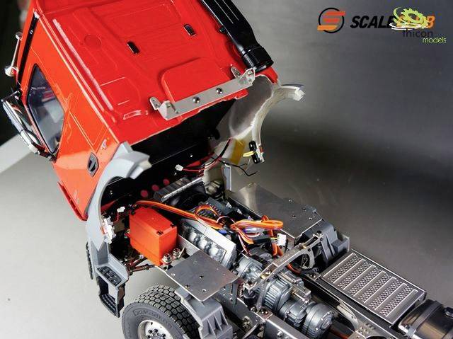 Roter Modell-LKW mit geöffneter Motorhaube, zeigt detaillierten Motor und Verkabelung. Markenlogos oben rechts.