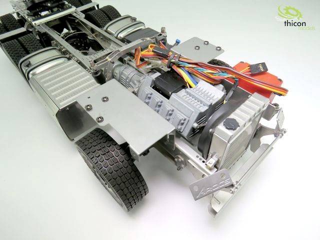 Ein Modell eines LKW-Chassis mit sichtbaren Bauteilen wie Motoren, Kabeln und Reifen, auf einer weißen Oberfläche gezeigt.