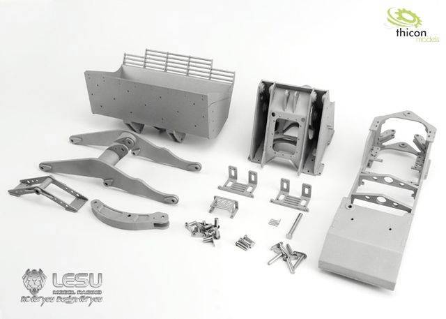 Bauteile eines Modellfahrzeugs aus Metall, inklusive Rahmen, Aufhängung und anderer Kleinteile, auf einer weißen Oberfläche ausgebreitet.