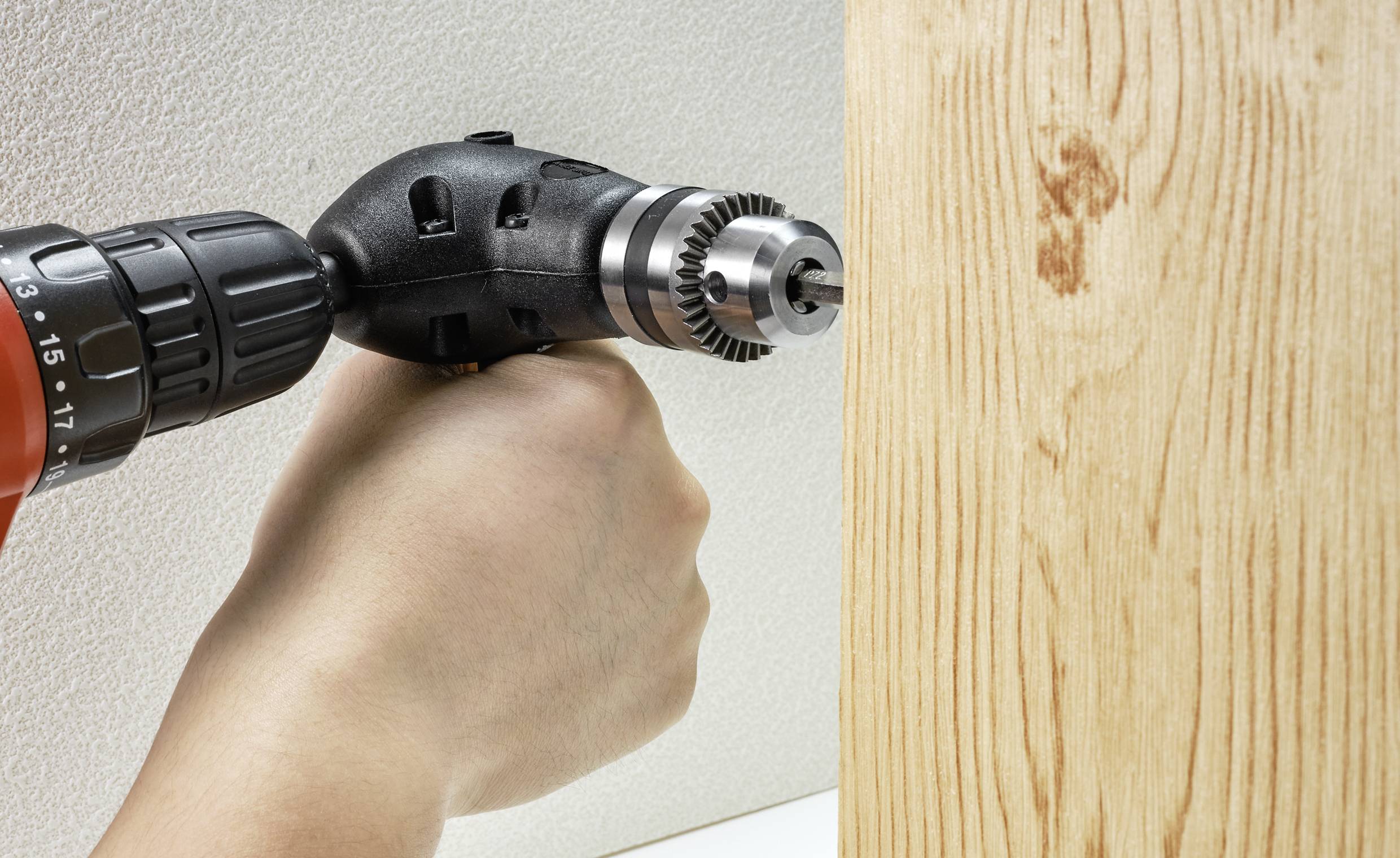 Eine Hand hält eine Bohrmaschine, die ein Loch in ein Stück Holz bohrt.