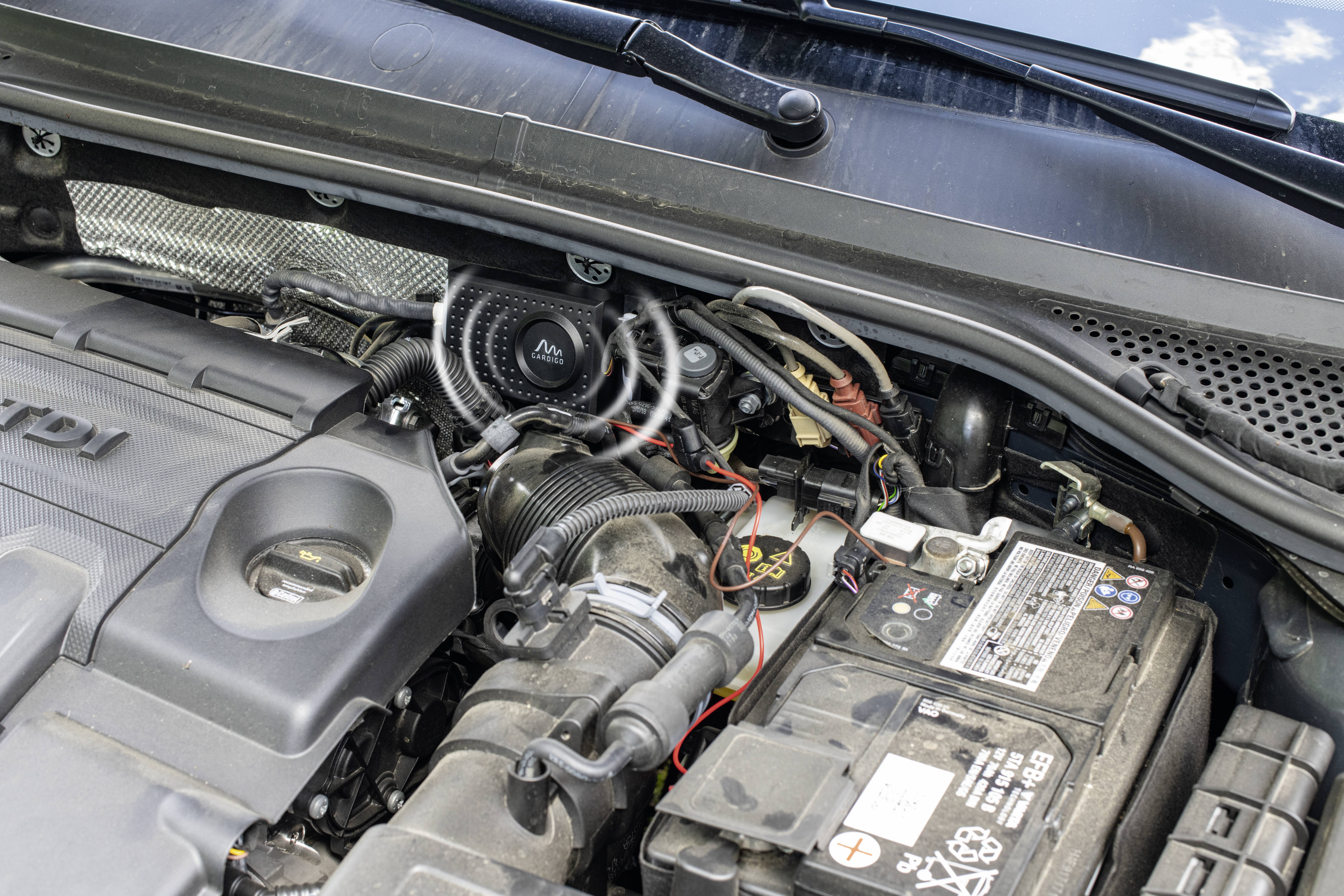 Auto-Motorraum mit sichtbarer Batterie, Motorblock und Kabeln. Fokus auf funktionale Komponenten und Anschlussdetails. 