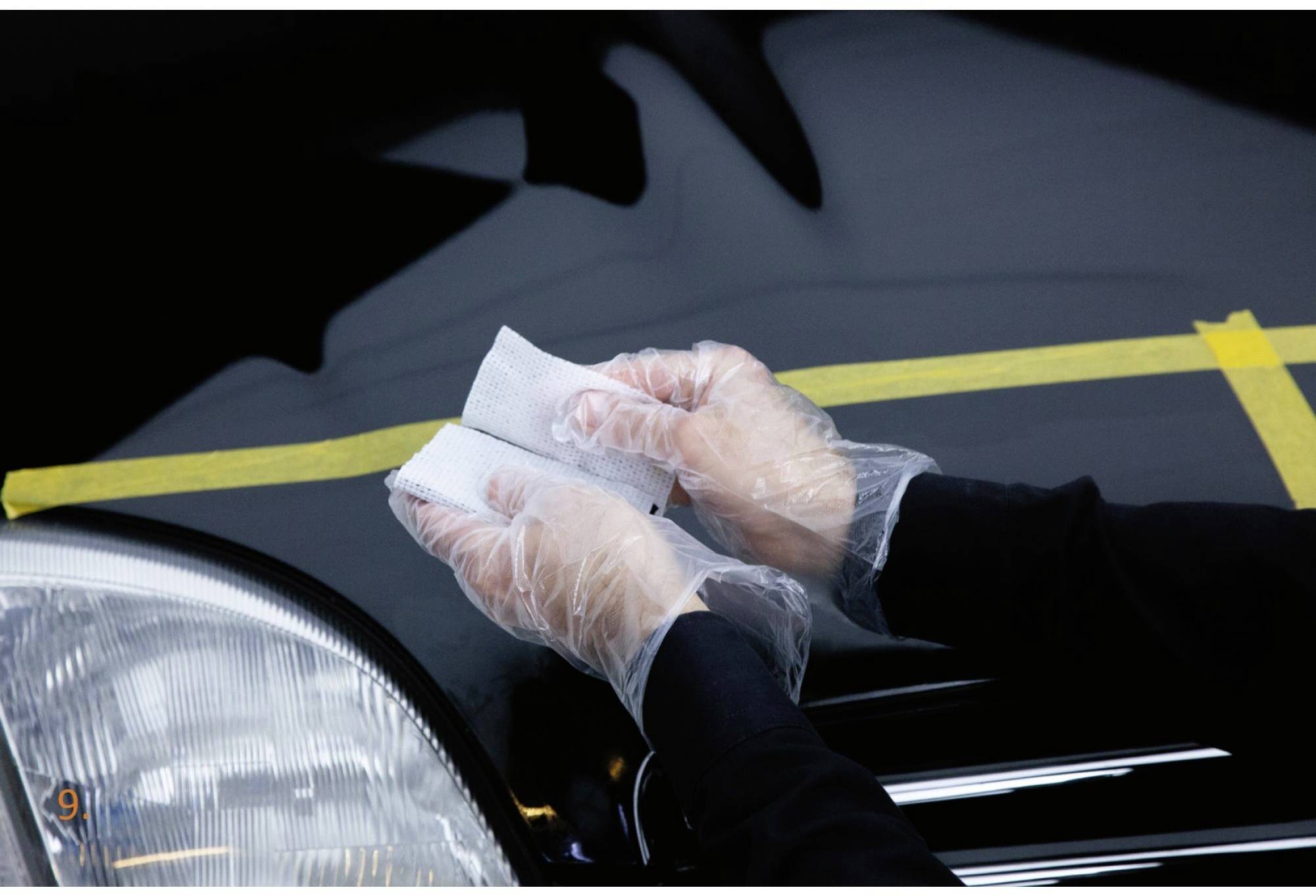Hände in Plastikhandschuhen polieren die Motorhaube eines Autos mit einem Tuch.
