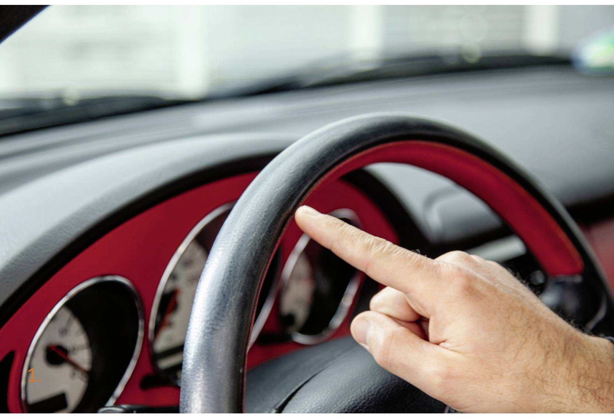 Eine Person zeigt mit dem Finger auf das Lenkrad eines Autos, im Vordergrund, detaillierte Ansicht.