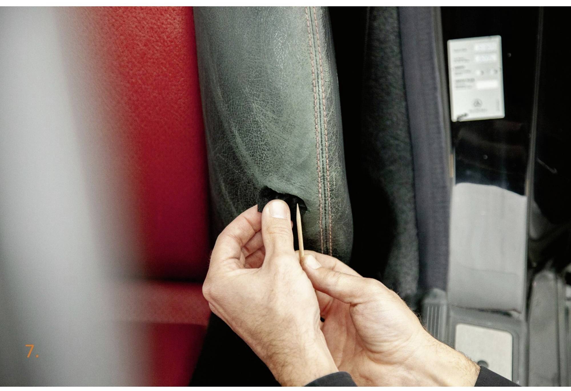 Eine Person hält einen Autositzbezug, hebt eine Lasche an, um den Bezug zu öffnen. Der Hintergrund zeigt ein rotes und schwarzes Material.