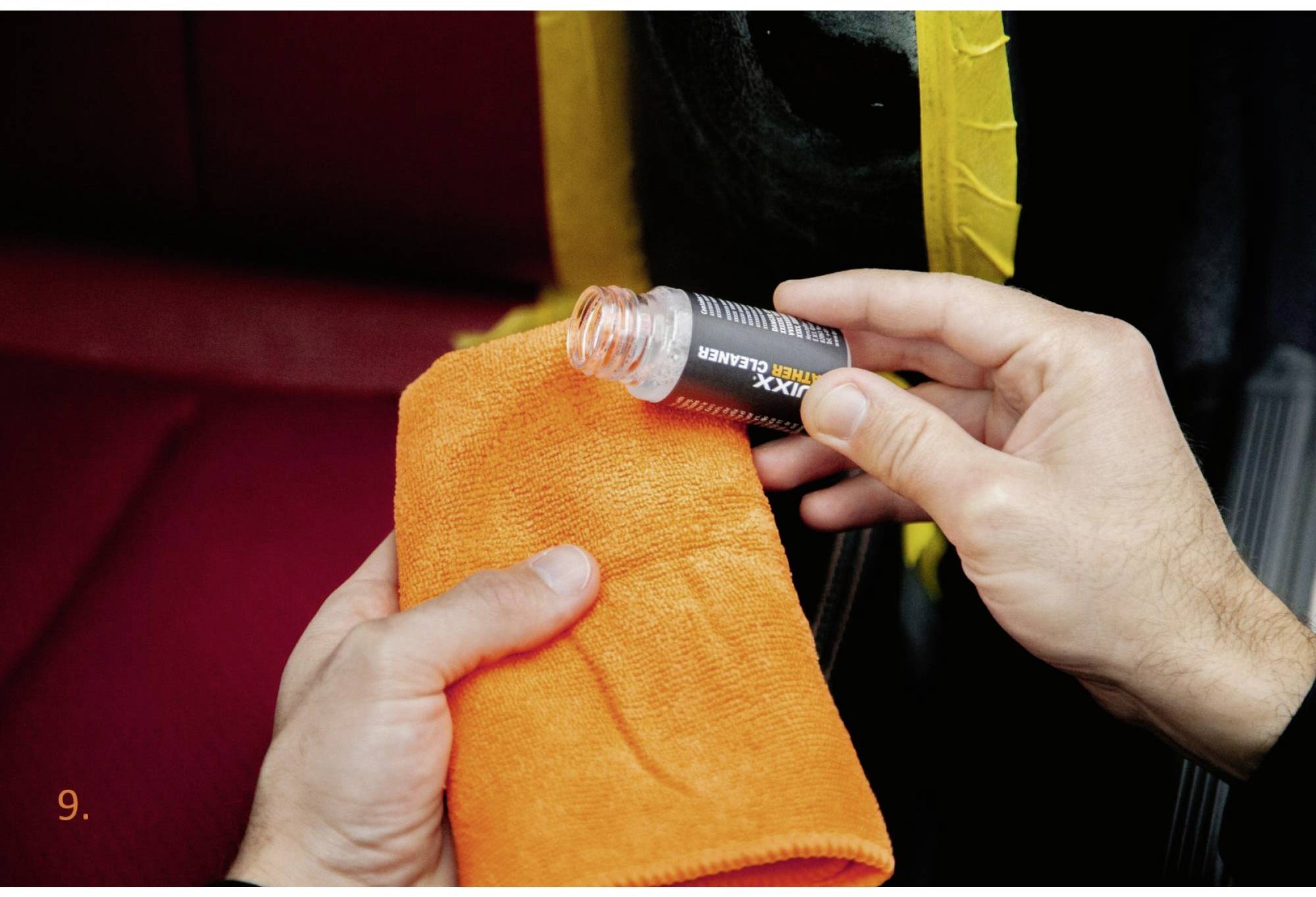 Person hält eine kleine Flasche mit 'Vinyl Cleaner' und ein orangefarbenes Tuch, reinigt eine mit gelbem Klebeband geschützte Stelle im Auto.