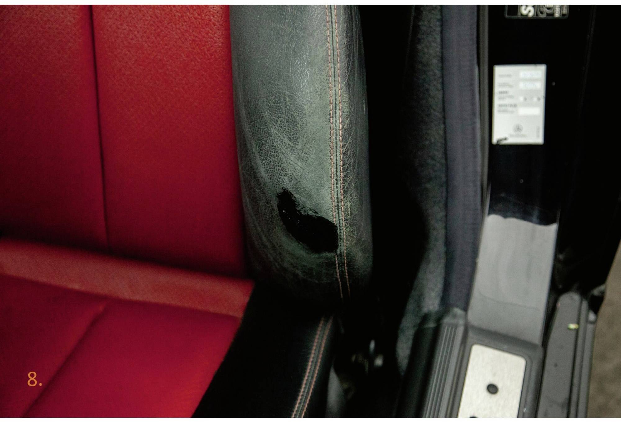 Beschädigte Autositzecke mit abgenutztem schwarzen Leder und darunter sichtbarem roten Polster, nahe Autotürbereich.