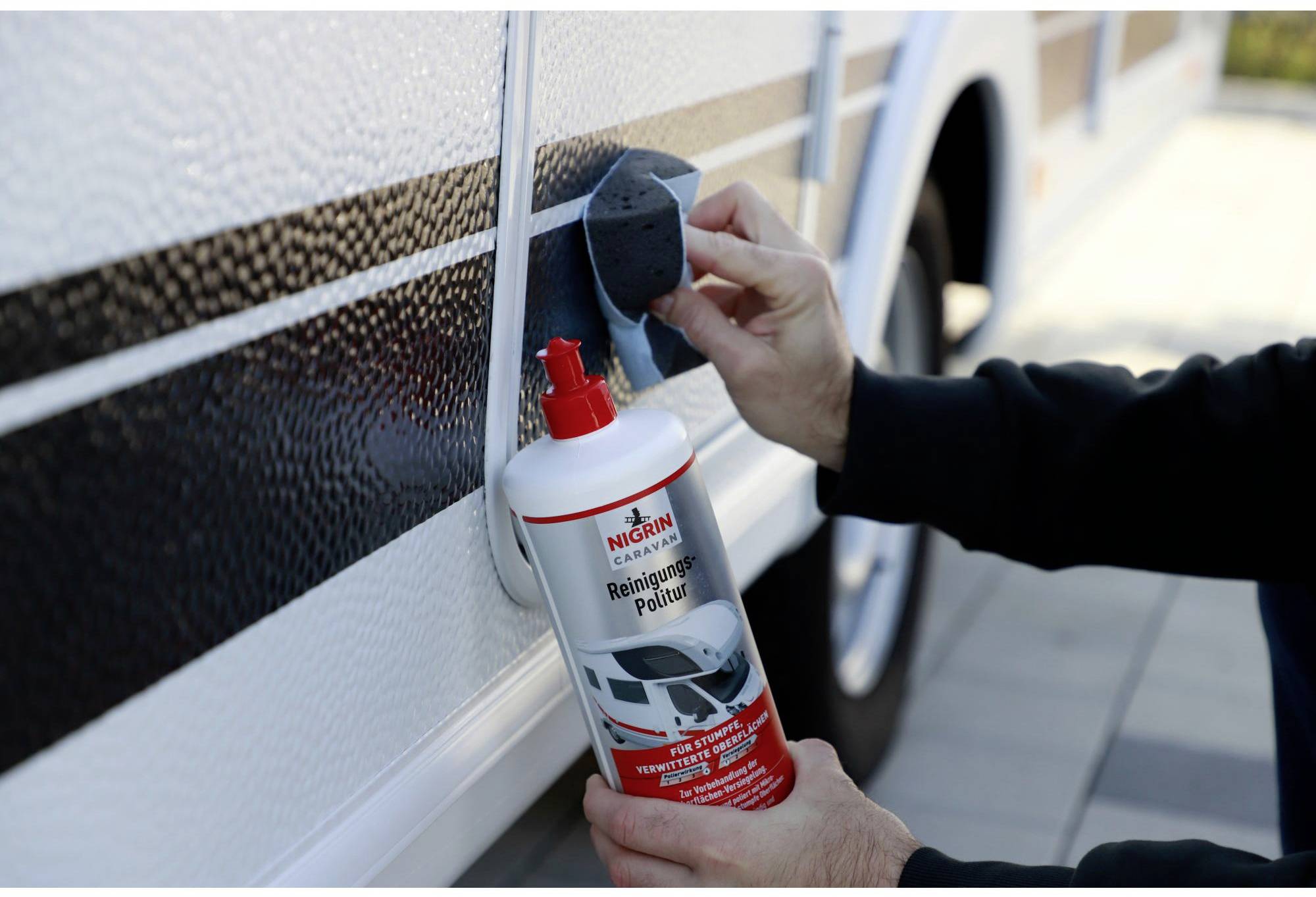 Eine Person reinigt einen weißen Wohnwagen mit einem Reinigungs- und Poliermittel. Eine rote Flasche mit einem Schwamm wird verwendet.