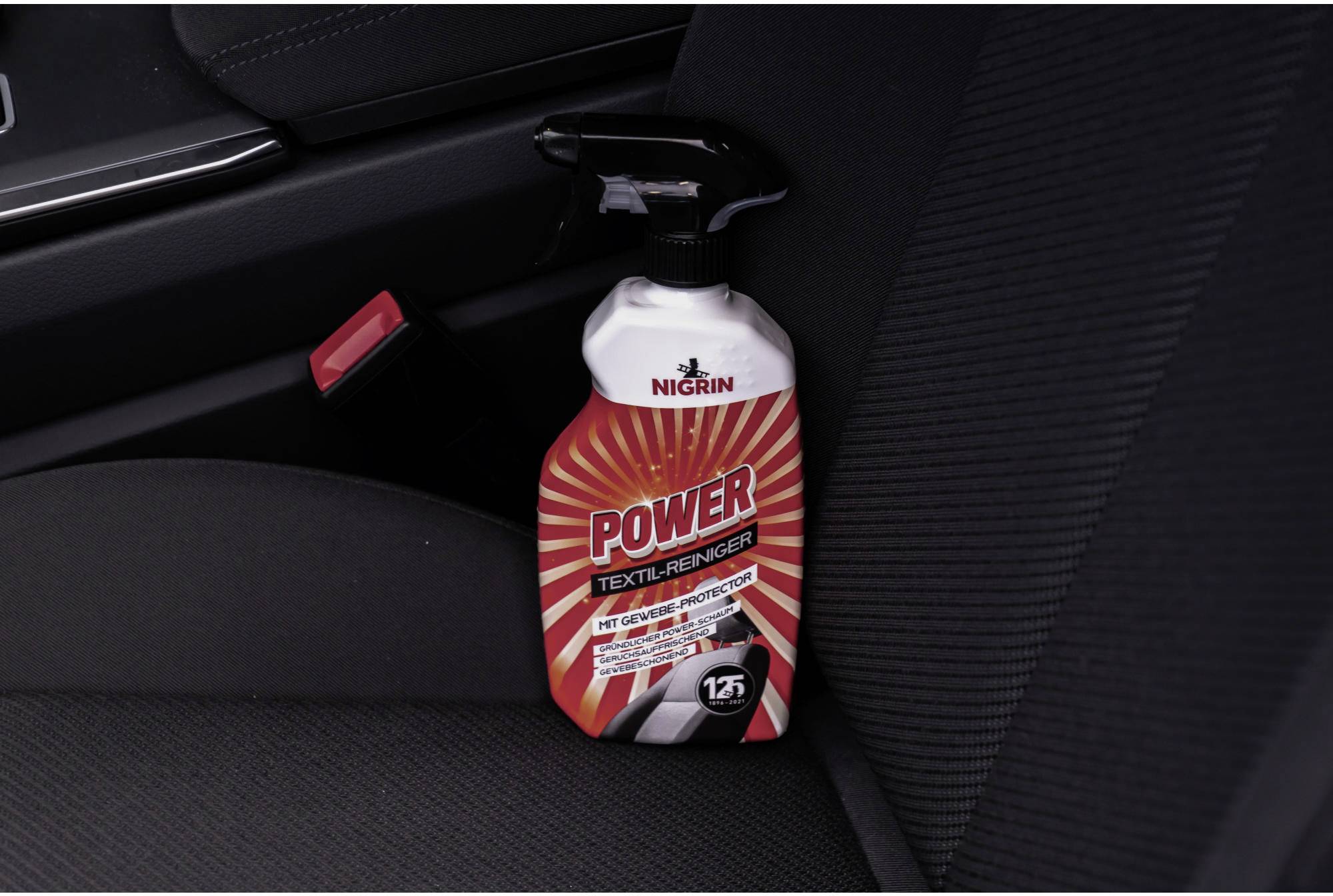 'Power Textil-Reiniger' Flasche auf einem Autositz, positioniert nahe einem Sicherheitsgurt. Reiniger für Autopolsterreinigung.