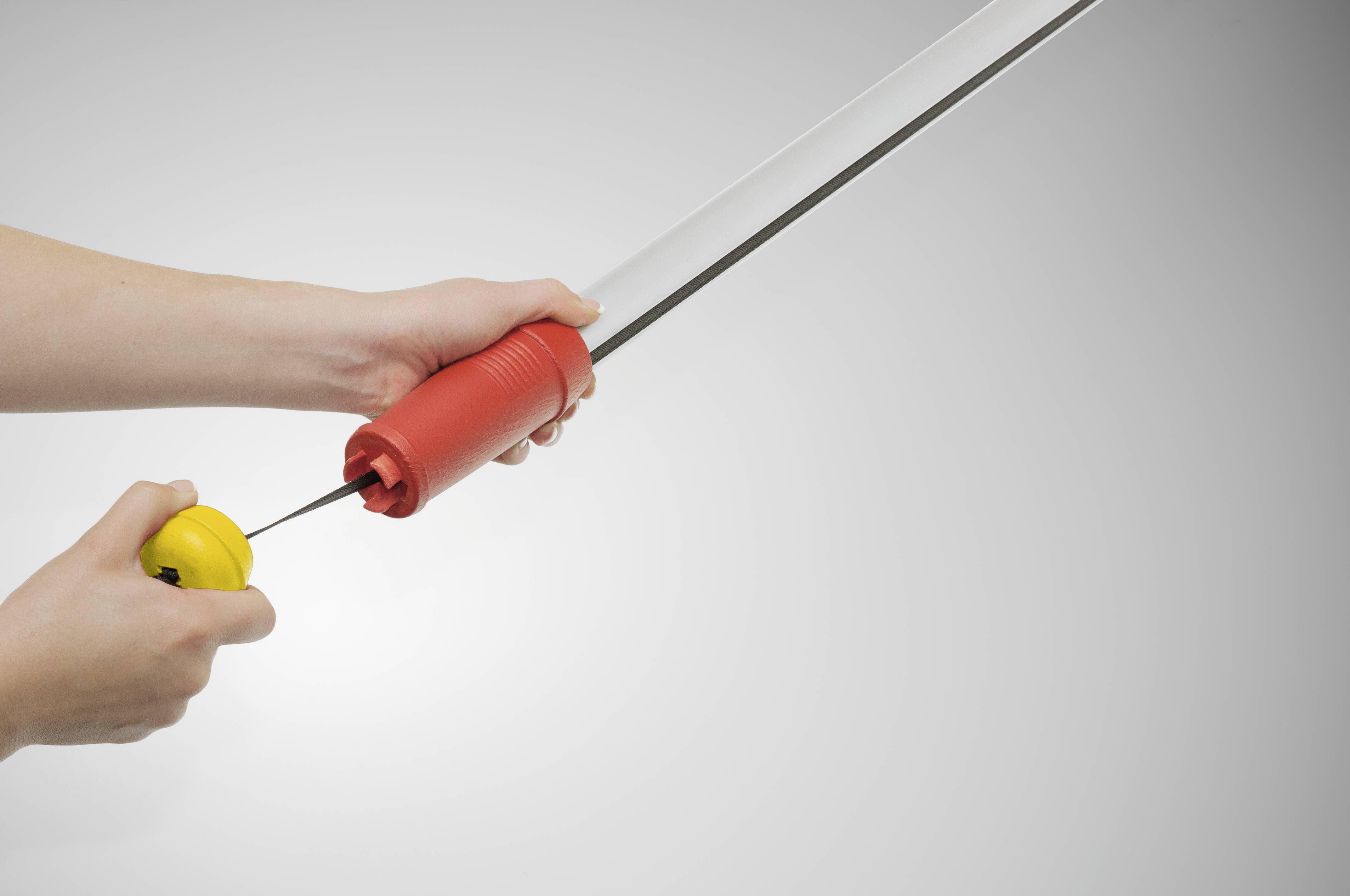 Eine Person hält ein rotes und gelbes Gerät, das wie ein langer, zylindrischer Gegenstand aussieht, in der Hand vor einem grauen Hintergrund.