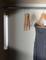 Kleiderschrank mit Kleiderstange, leuchtender Lichtquelle und einigen leeren Kleiderbügeln. Ein graues Kleid hängt rechts.