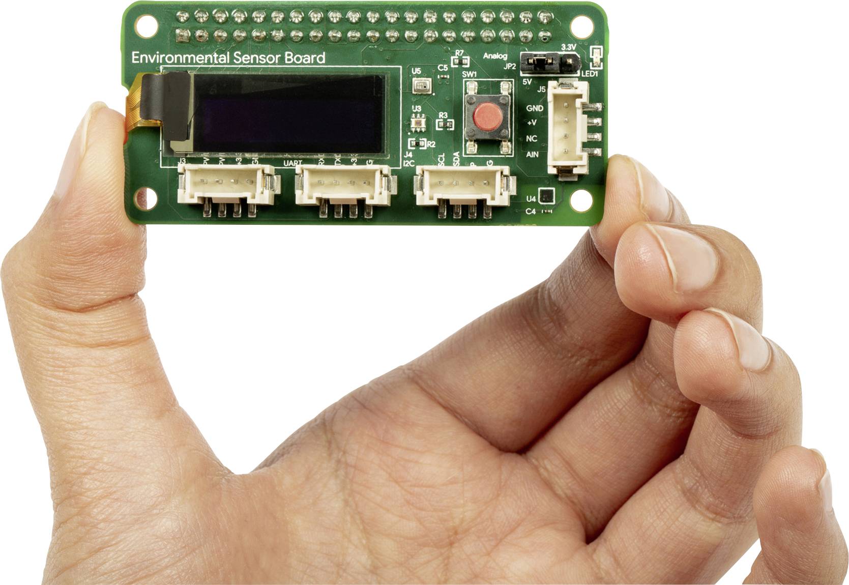 'Environmental Sensor Board' mit Display und Anschlüssen, von Hand gehalten. Zeigt elektronische Komponenten für Umweltdatenüberwachung.