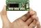 'Environmental Sensor Board' mit Display und Anschlüssen, von Hand gehalten. Zeigt elektronische Komponenten für Umweltdatenüberwachung.