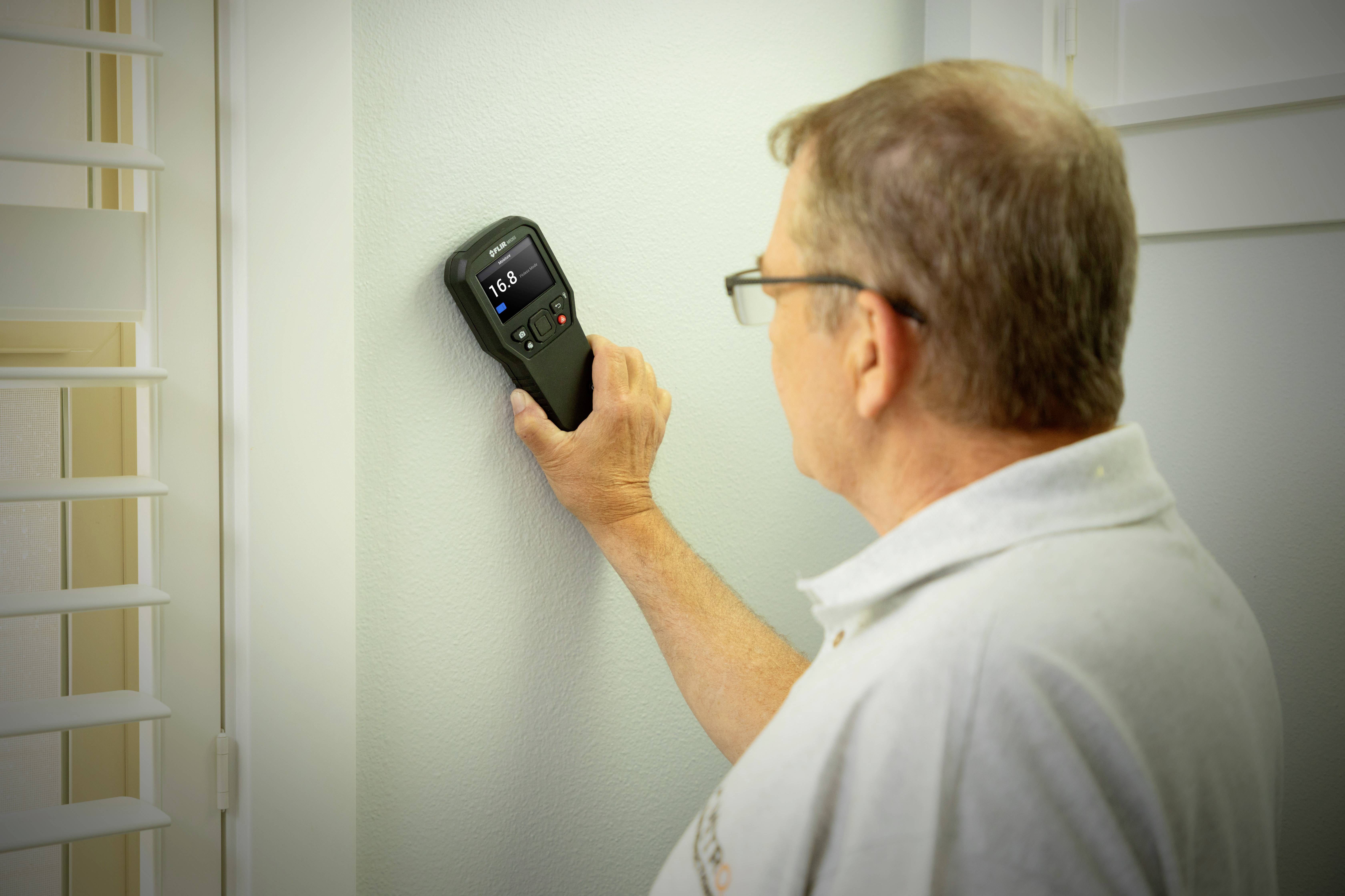 Ein Mann prüft mit einem digitalen Gerät die Wandstärke in einem Raum, möglicherweise zur Vorbereitung eines Bau- oder Renovierungsprojekts.