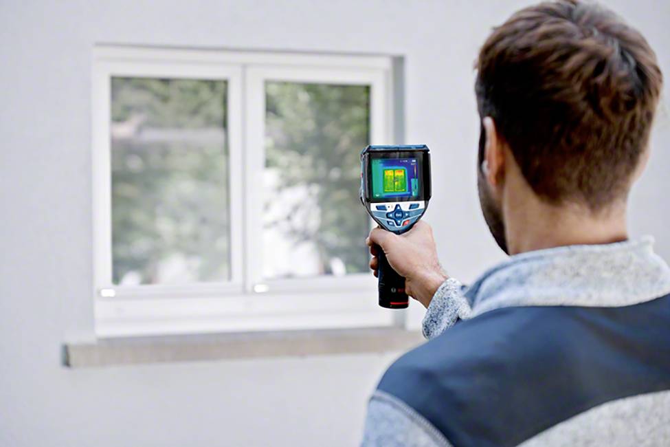 Ein Mann hält eine Wärmebildkamera auf ein Fenster gerichtet, um die Wärmeisolierung zu überprüfen.