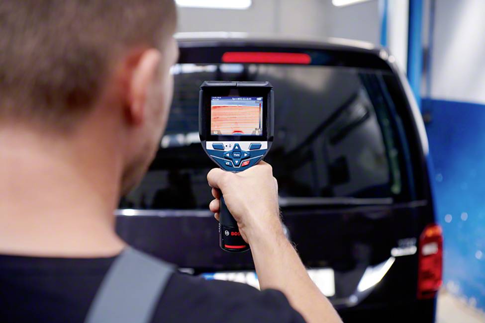 Ein Mann misst mit einem digitalen Gerät die Temperaturen auf einem schwarzen Fahrzeug, möglicherweise zur Überprüfung oder Wartung.