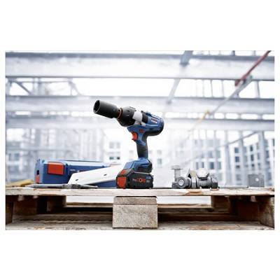 Eine kabellose Bohrmaschine mit Bohrern, die auf einer Holzpalette in einer industriellen Bauumgebung mit Stahlrahmenwerk im Hintergrund platziert ist.