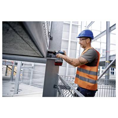 Ein Bauarbeiter mit blauem Schutzhelm und orangefarbener Warnweste benutzt einen Akkuschrauber an Metallträgern im Inneren eines sich im Bau befindenden Gebäudes.
