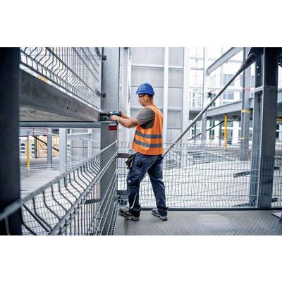 Ein Bauarbeiter mit Helm und Warnweste arbeitet mit einem Werkzeug an einer Stahlkonstruktion auf einer Baustelle.