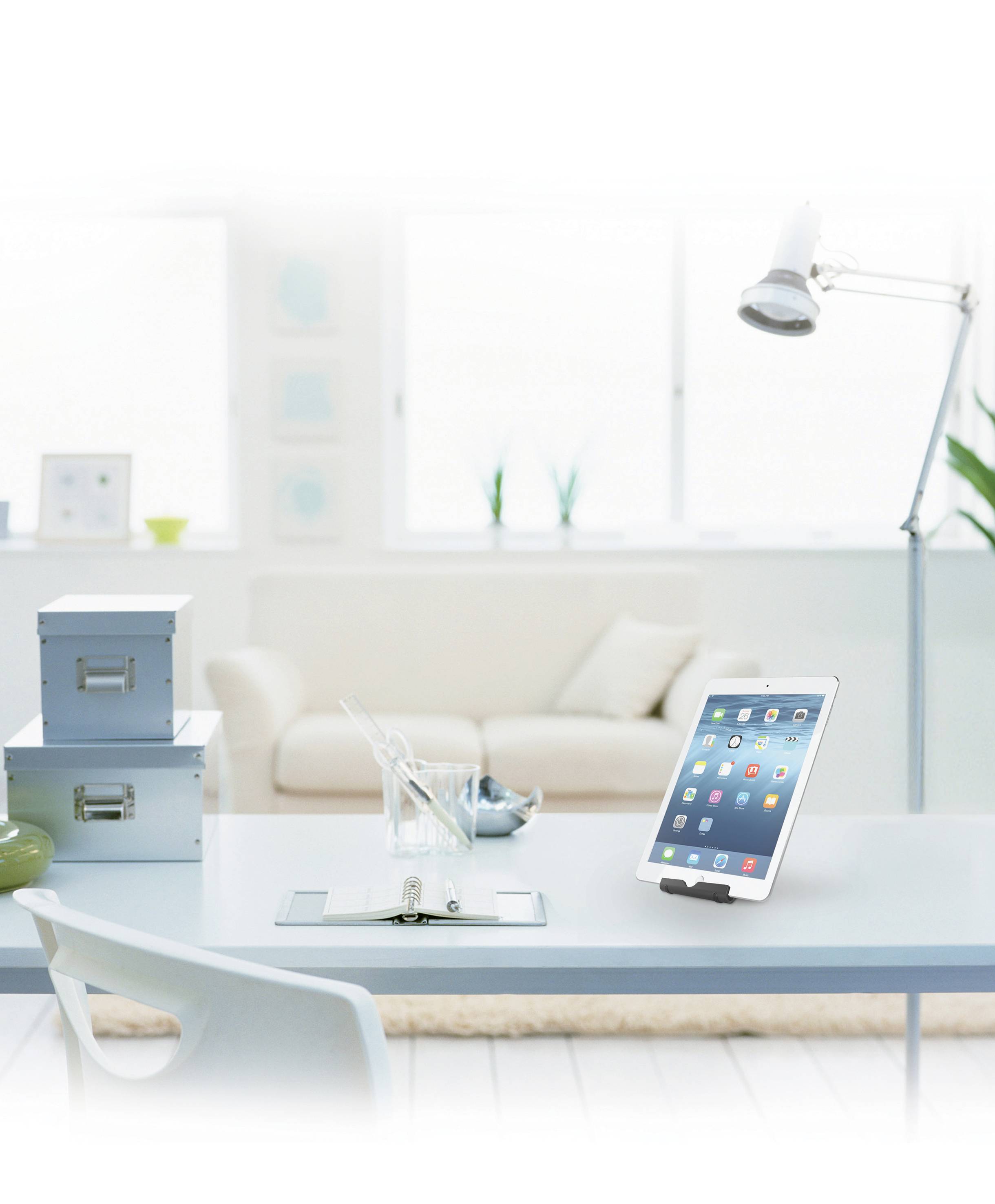 Ein Tablet auf einem Schreibtisch in einem hellen Raum. Im Hintergrund sind ein Sofa, eine Stehlampe und Pflanzen zu sehen.