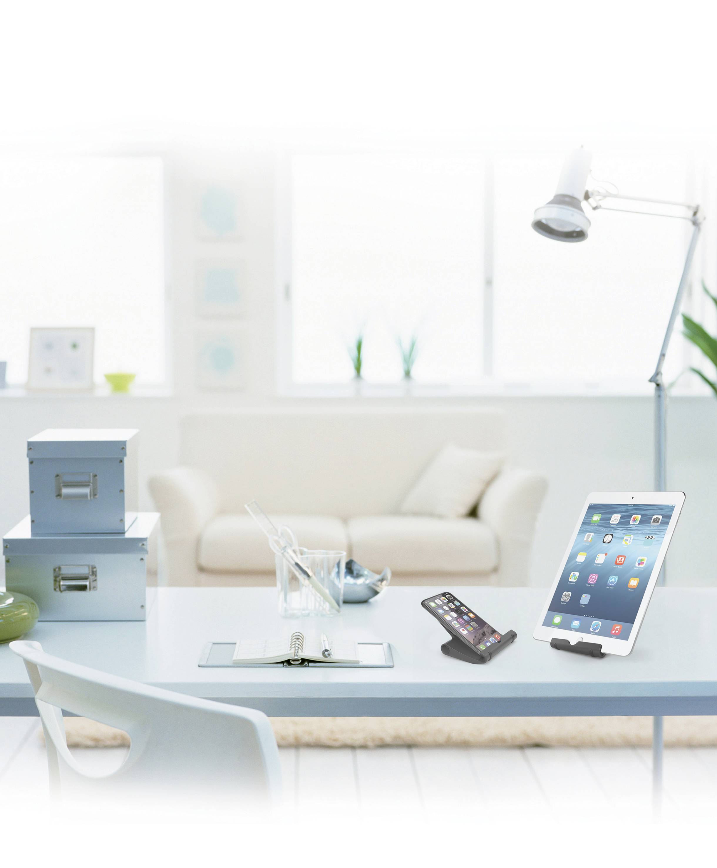 Helles, modernes Wohnzimmer mit einem Schreibtisch, auf dem ein Tablet, ein Smartphone und Büroartikel stehen. Im Hintergrund ein Sofa.