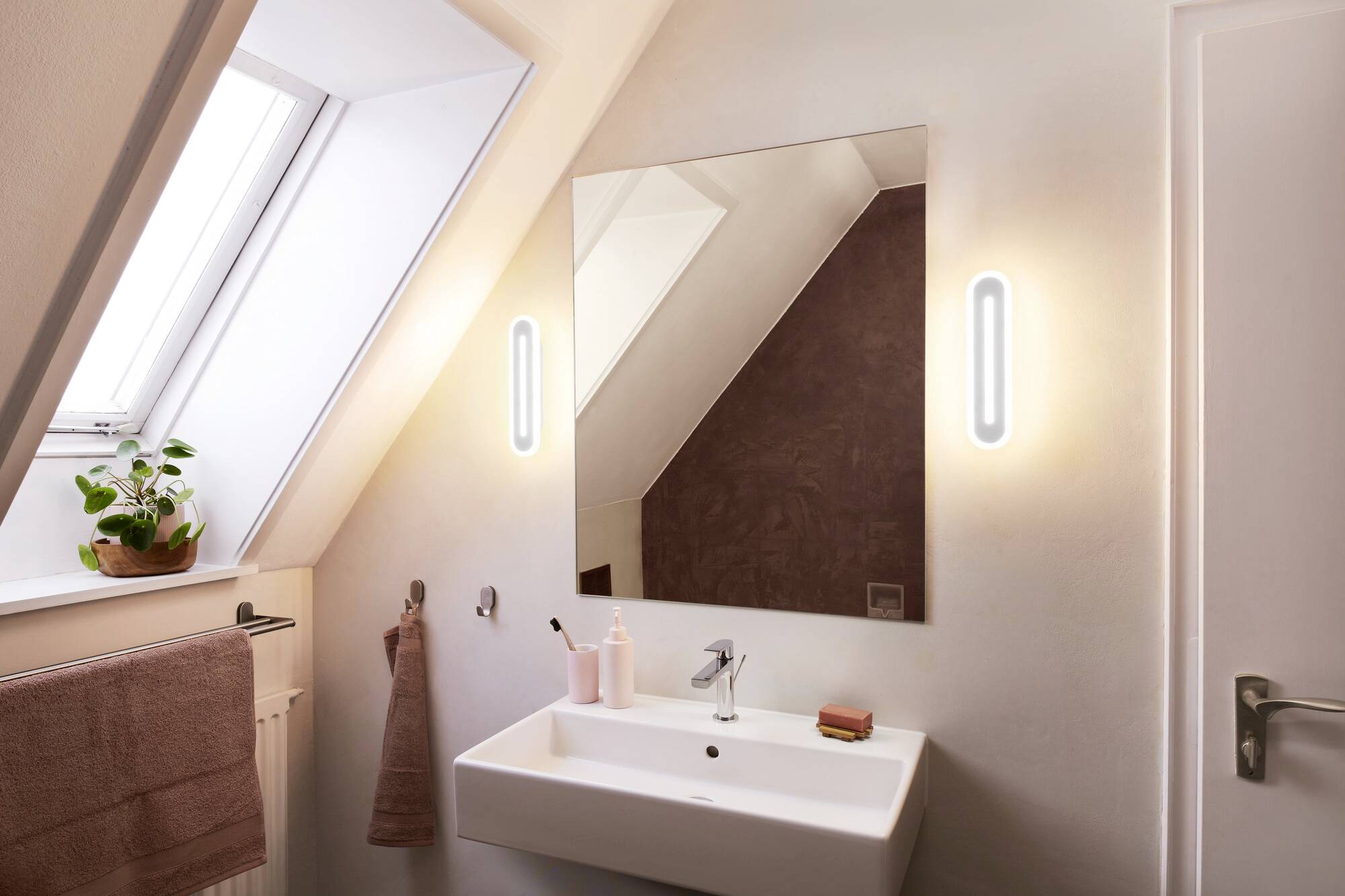 Ein modernes Badezimmer mit Waschbecken, rechteckigem Spiegel und minimalistischem Dekor. Pflanzen und Handtücher ergänzen den Raum.