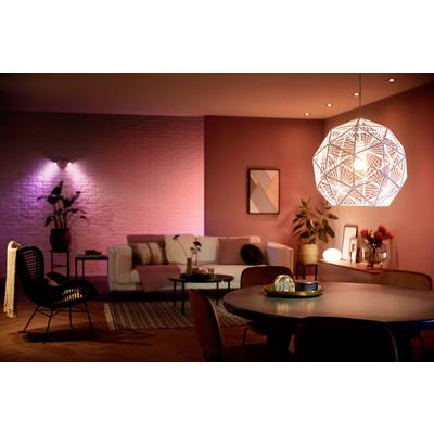 Ein modern eingerichtetes Wohnzimmer mit einem runden Tisch im Vordergrund. Eine geometrische Pendelleuchte beleuchtet den Raum.