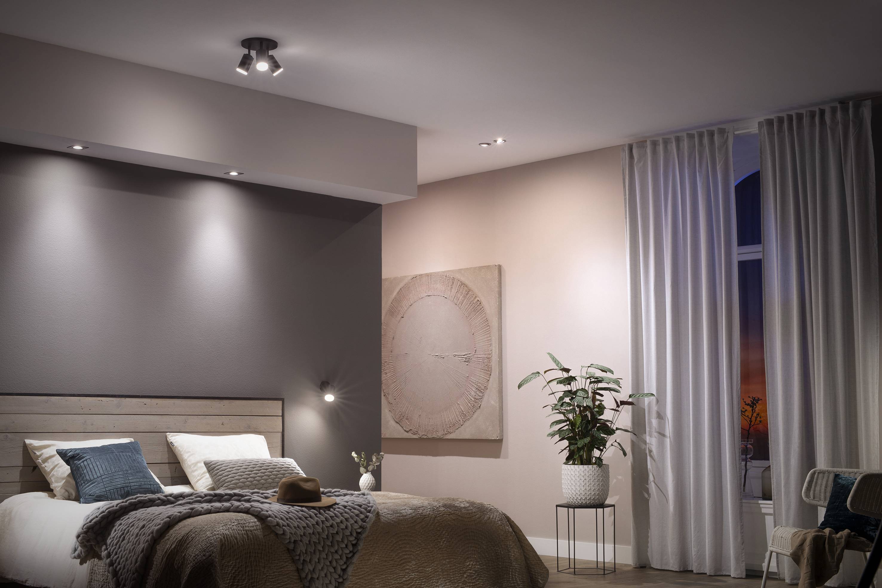 Gemütliches Schlafzimmer mit Doppelbett, grauen und beigen Wänden, Vorhängen und Zimmerpflanze. Wandbild bei weicher Beleuchtung.