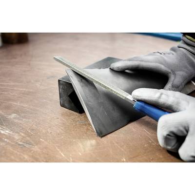Eine Person in grauen Handschuhen feilt ein Metallstück auf einer Arbeitsplatte.