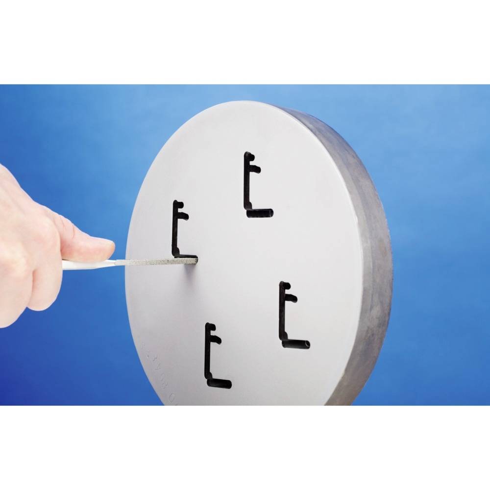 Ein rundes Metallwerkzeug mit vier L-förmigen Schneiden; eine Hand hält einen Messstab an die Oberfläche zum Messen oder Anpassen.