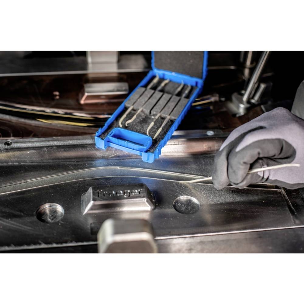 Eine Person in Arbeitshandschuhen platziert einen Draht in eine Metallvorrichtung, daneben liegt eine offene blaue Box mit weiteren Drähten.