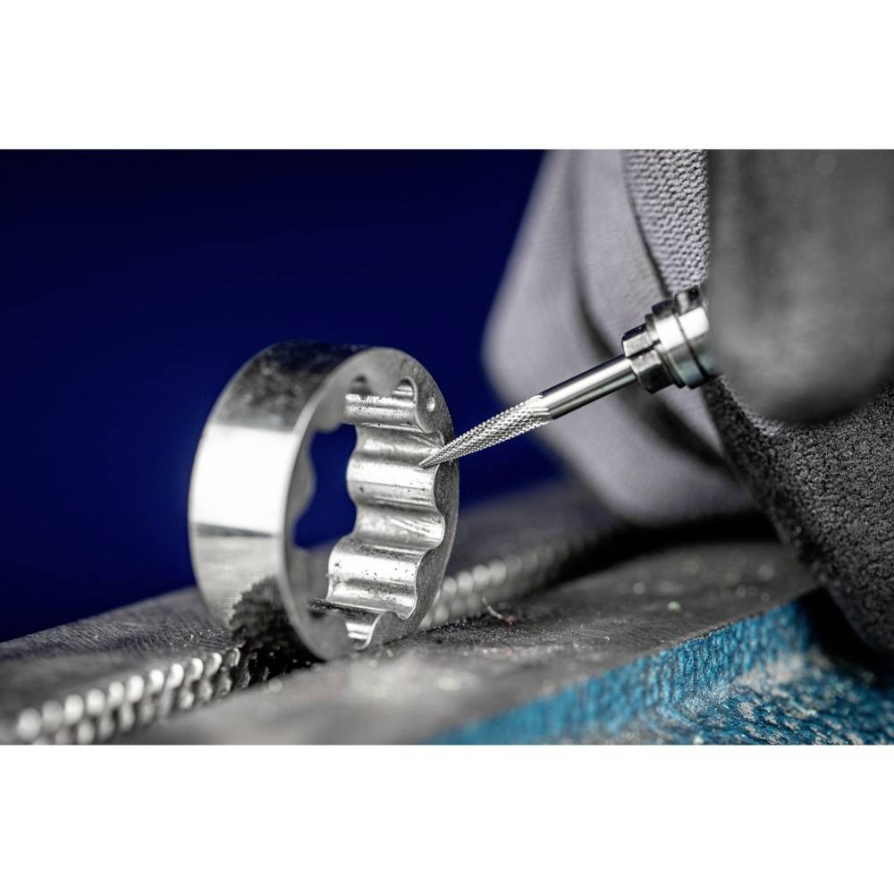 Eine Metallfräsmaschine bearbeitet einen runden Metallring, der in einem Schraubstock befestigt ist. Eine Hand führt den Fräsvorgang aus.