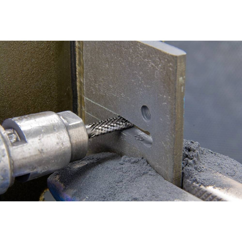 Nahaufnahme einer Metallbohrmaschine, die ein Loch in ein dickes Metallstück bohrt. Staub und Späne sind sichtbar um die Maschine.
