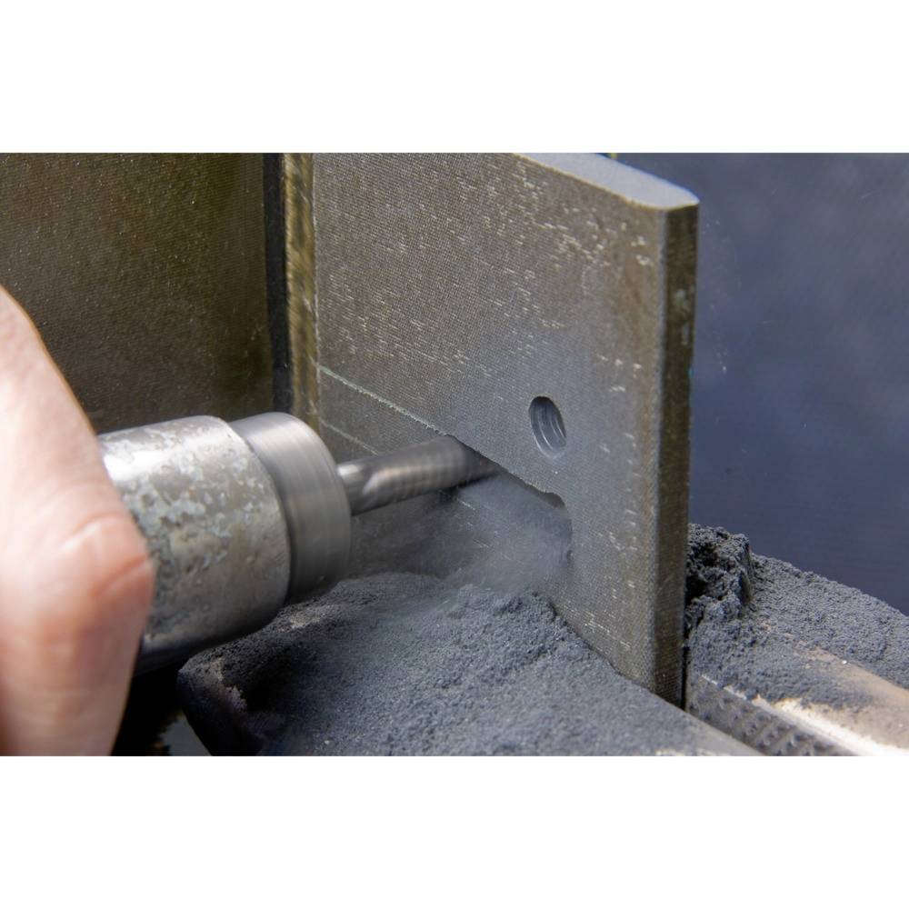 Eine Hand hält ein rotierendes Werkzeug, das ein Loch in eine Metallplatte bohrt. Staub und Späne sind sichtbar.