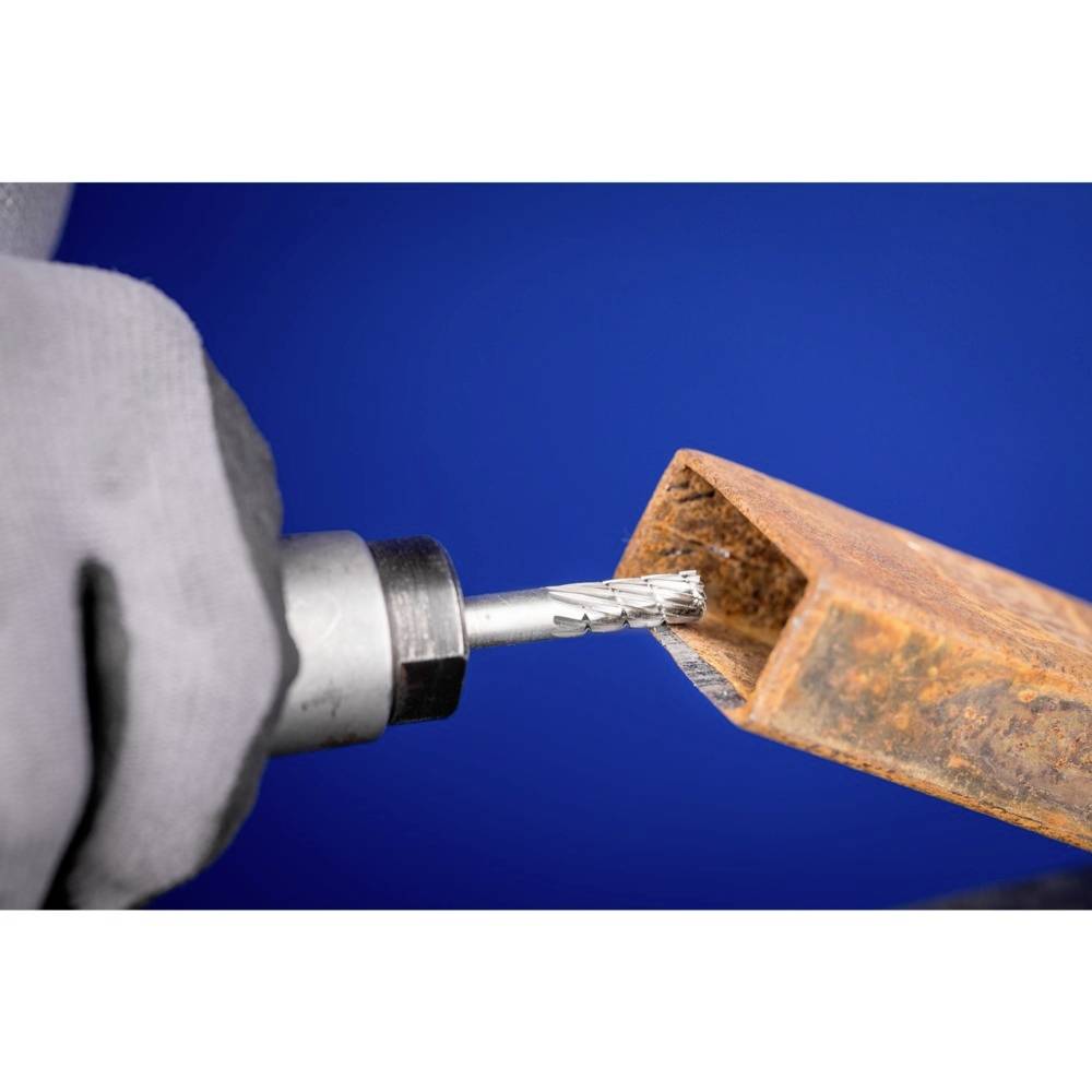 Eine Person bohrt ein rechteckiges Metallrohr mit einer Bohrmaschine vor blauem Hintergrund.