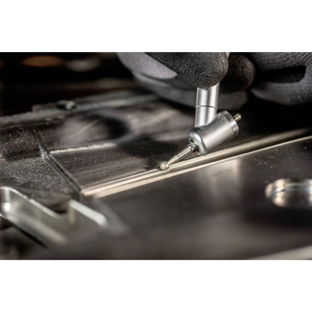 Eine Nahaufnahme zeigt eine Person, die mit einem kleinen Werkzeug eine Metalloberfläche bearbeitet, möglicherweise in einem Fertigungsprozess.