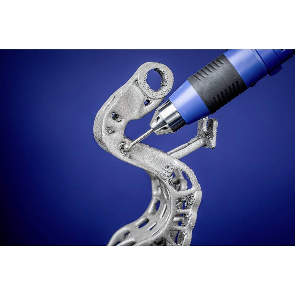 Ein 3D-Drucker druckt ein komplexes, geschwungenes Metallobjekt mit blauer Düse auf blauem Hintergrund.