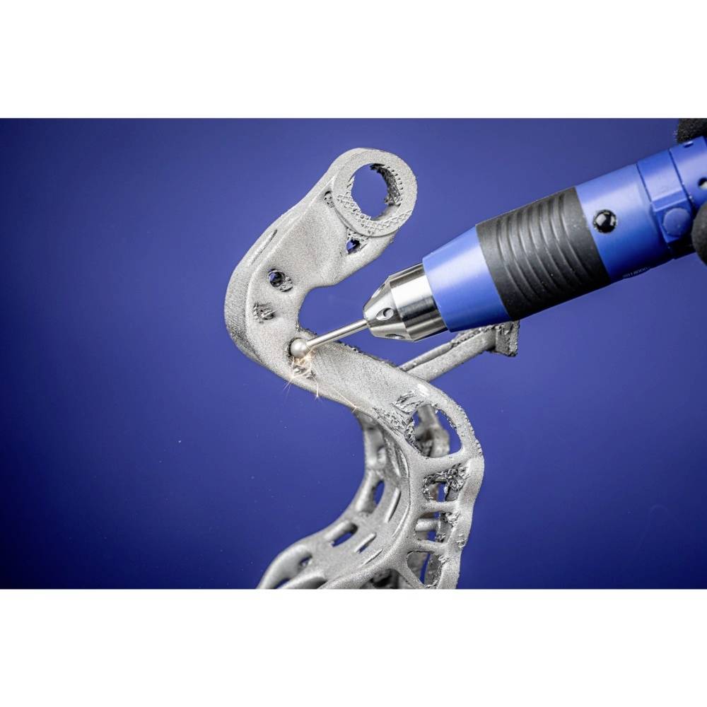 3D-gedrucktes Metallteil wird mit einem blauen Dremel-Werkzeug poliert, vor blauem Hintergrund.