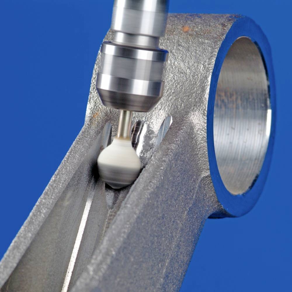 Ein Metallschneider bearbeitet präzise die Oberfläche eines metallischen Werkstücks vor blauem Hintergrund.