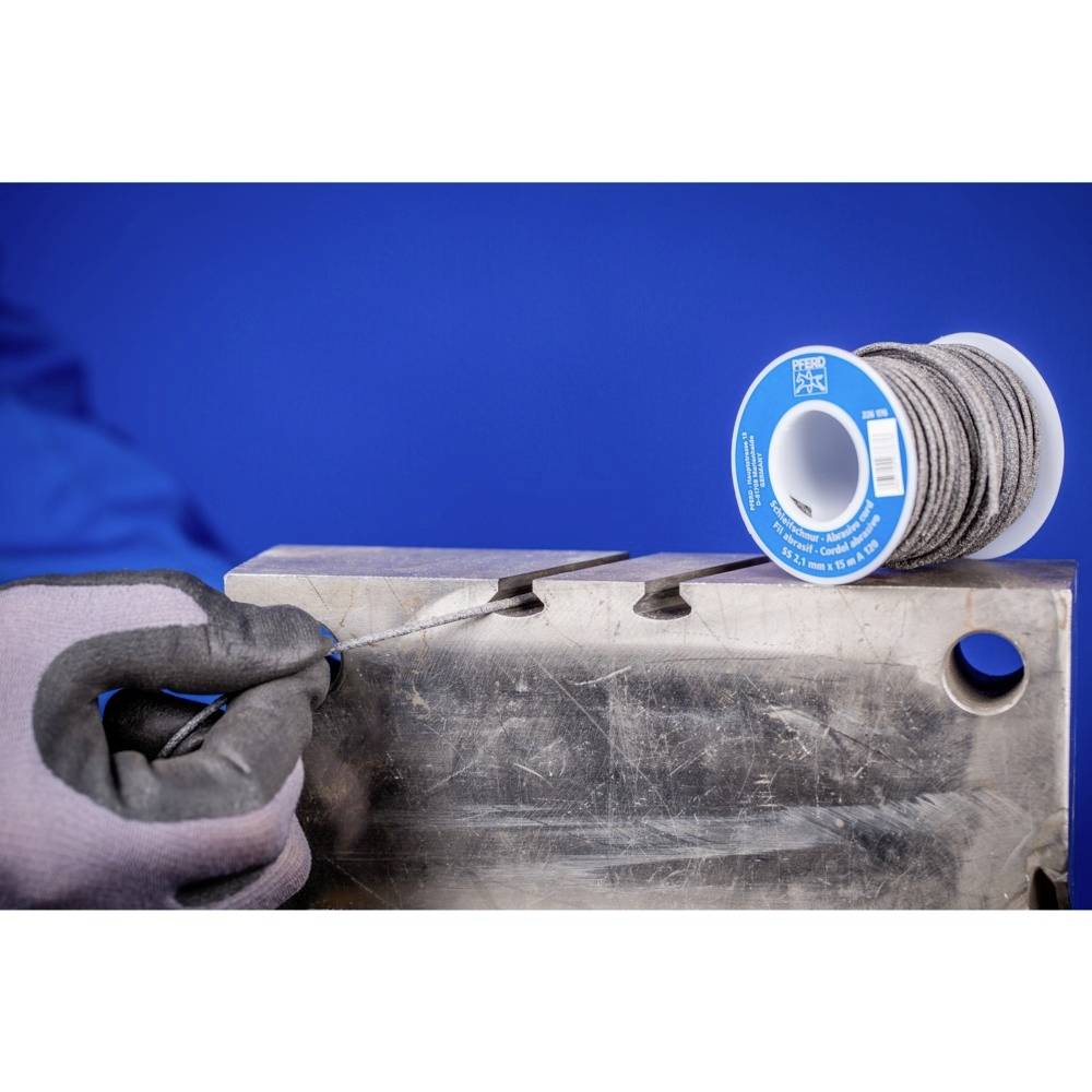 Ein Metallblock mit einer gezackten Kante, an der eine Person ein Stahlseil schneidet. Daneben eine Rolle des aufgewickelten Seils.