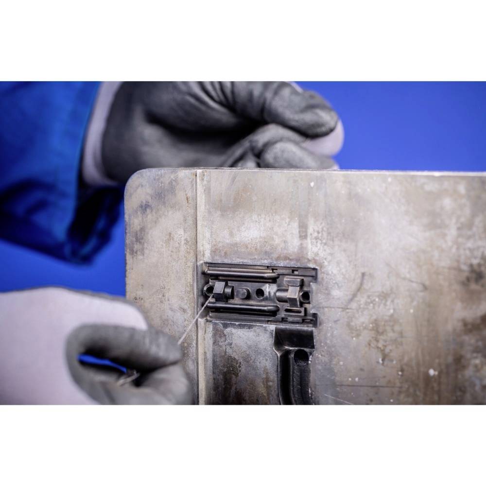 Eine Person in Handschuhen arbeitet präzise an einer alten Metalloberfläche mit einem kleinen Werkzeug.