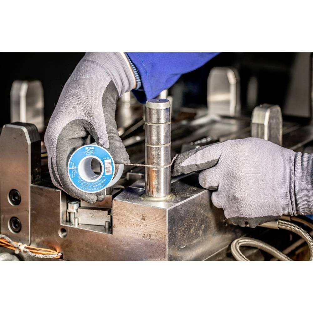 Zwei behandschuhte Hände wickeln einen Draht um ein zylindrisches Metallteil in einer Werkstattumgebung.