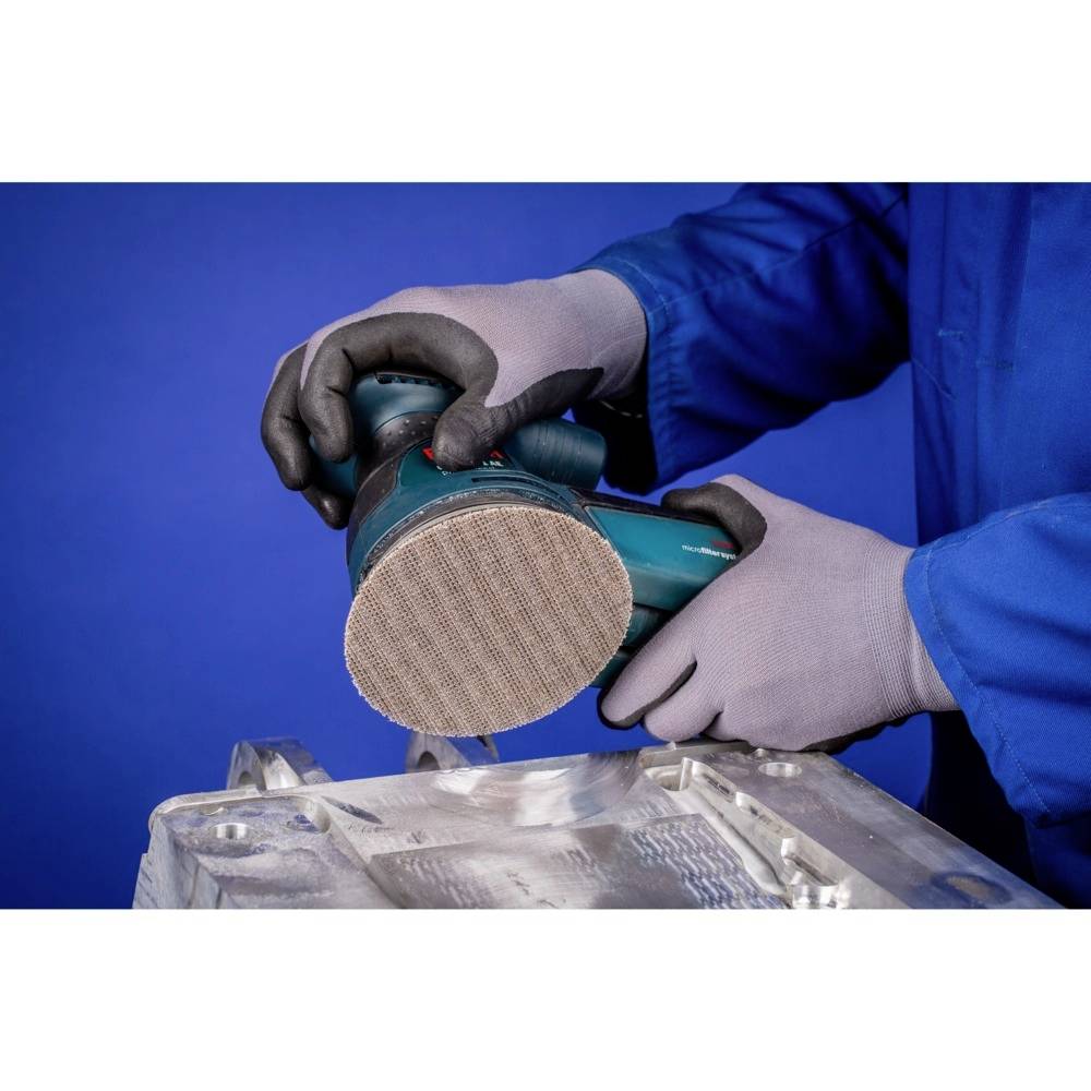 Eine Person schleift mit einem elektrischen Schleifgerät eine metallene Oberfläche. Der Hintergrund ist blau.