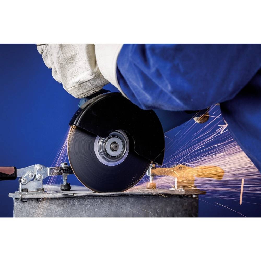 Arbeiter in blauer Jacke schneidet Metall mit Winkelschleifer, sprühende Funken. Sicherheitshandschuhe und blauer Hintergrund sichtbar.