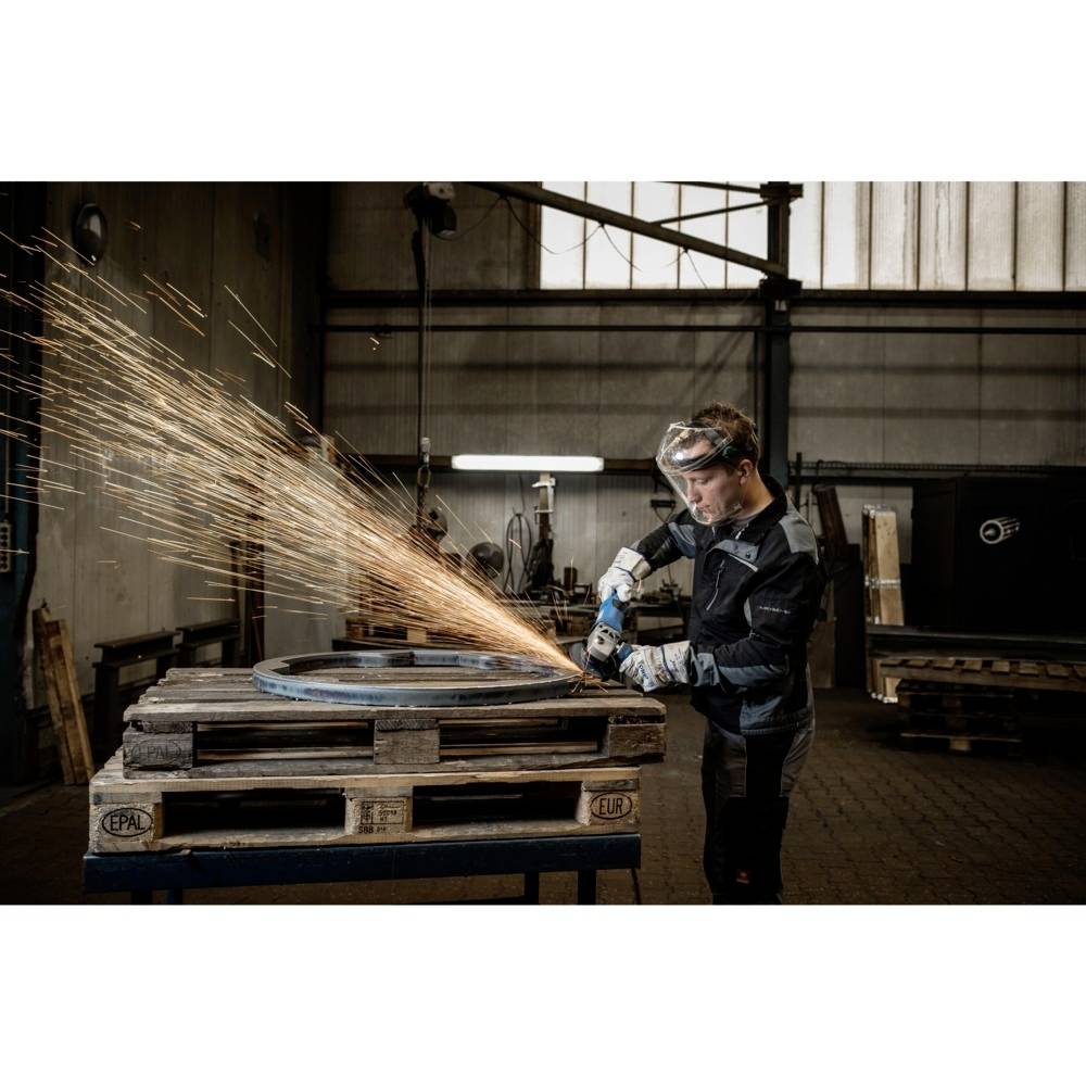 Person in Schutzkleidung schleift Metall mit einem Winkelschleifer, Funken sprühen. Umgebung zeigt eine industrielle Werkstatt.